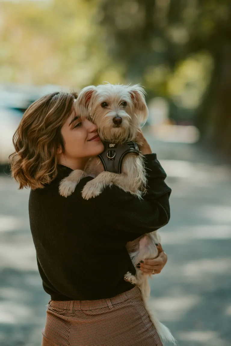 Woman holding a small white dog — comparing the cheapest pet insurance for dogs starts with understanding plan terms
